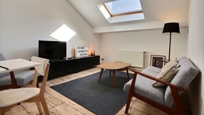 Un espacio habitable estilo loft acogedor con tragaluz, televisor de pantalla plana, una mesita y un sofá.