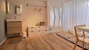 Un baño moderno con tocador de madera, un espejo, un perchero y una ventana con cortinas de gasa.