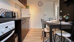 Una cocina compacta con electrodomésticos modernos, un comedor con una mesa preparada para dos personas y un reloj en la pared.