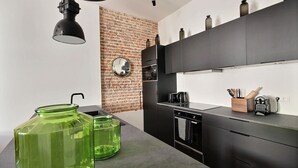 Una cocina moderna con pared de ladrillo decorativa, armarios negros y frascos de vidrio verde sobre la encimera.