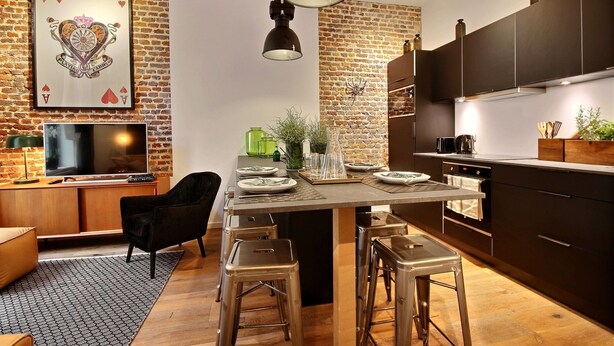 Una cocina moderna con pared de ladrillo, armarios oscuros y una isla central con taburetes.