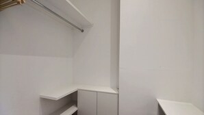 Un coin de pièce aux murs blancs, avec une armoire blanche et une étagère en bois.