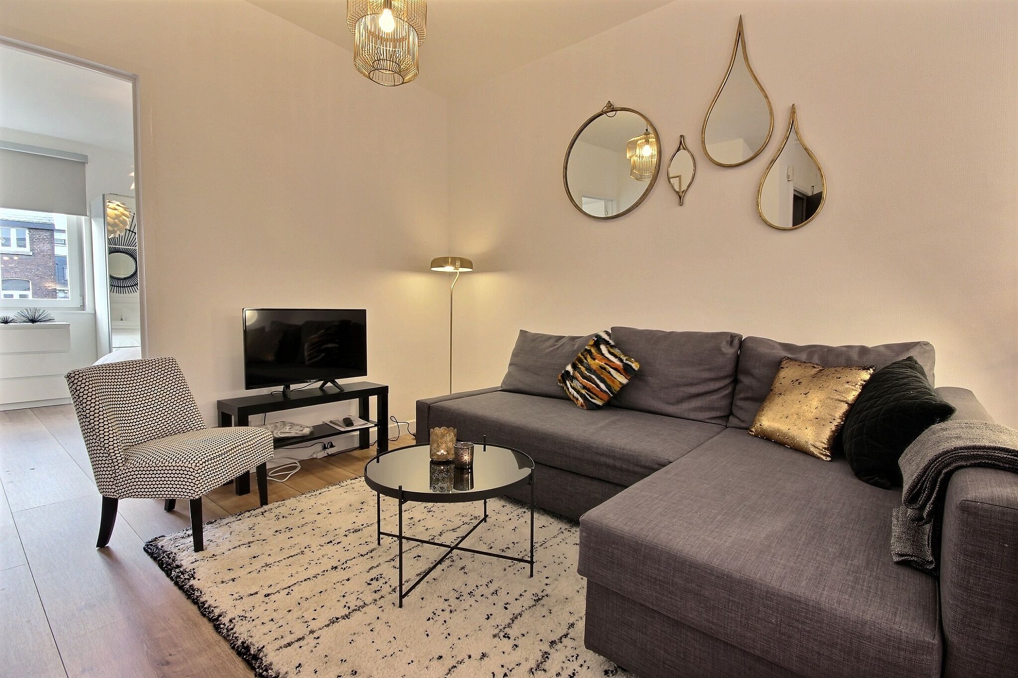 Una sala de estar moderna con un sofá gris, un sillón estampado, una mesa de centro redonda y una lámpara de pie.