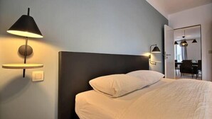 A hotel room with a bed, a bedside table, a lamp, and a mirror. - Chez Clarisses - 3 bedrooms (Liège)