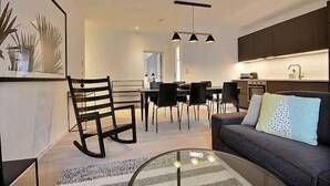 A modern living room with a sofa, a glass coffee table, and a dining area with chairs and a table. - Chez Clarisses - 3 bedrooms (Liège)