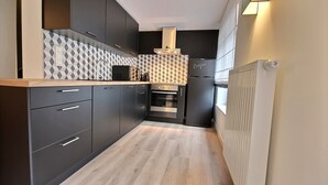 A modern kitchen with dark cabinetry, a patterned backsplash, and a built-in oven. - The KAT105 - 3 bedrooms (Liège)