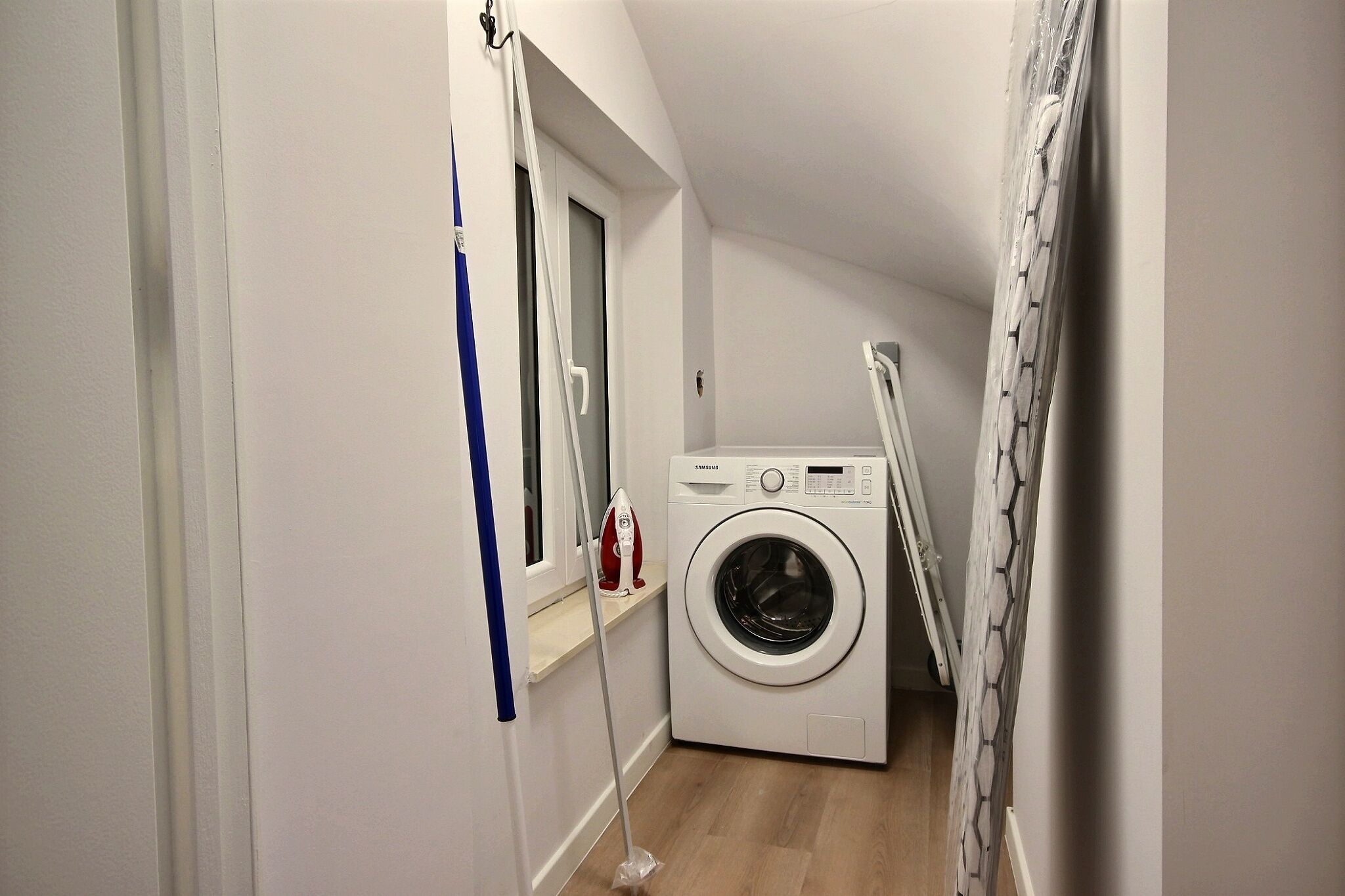 Ein kleiner Waschraum mit Waschmaschine, Wäscheständer und Fenster.