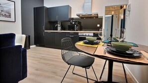 A modern kitchen with dark cabinets, a coffee machine, and a dining area with a table, chairs, and a bowl. - The KAT106 - 1 bedroom (Liège)