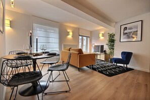 Een moderne woonkamer met een bank, stoelen, een eettafel met stoelen, een televisie en een plant.