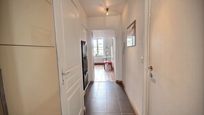 A hallway with a tiled floor, a refrigerator, and a dining area with a table and chairs. - Jardin Botanique - 1 bedroom (Liège)
