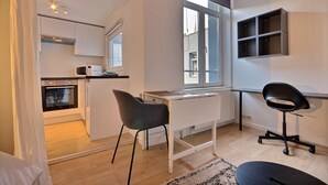 A compact living space with a kitchenette, a dining area with a table and chairs, and a workspace with a computer. - Le Studio 15 - Superb Studio in the city center (Liège)