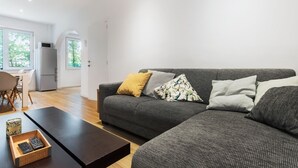 Ett modernt vardagsrum med en grå soffa, ett soffbord i trä och en liten köksdel i bakgrunden.