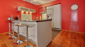 A modern kitchen with a red wall, white cabinets, a central island with stools, and a clock mural. - Rue des Ixellois - 2 bedrooms (Liège)