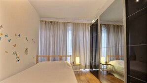 A hotel room with a large bed, a bedside table with a lamp, a mirror, and a window with curtains. - Rue des Ixellois - 2 bedrooms (Liège)