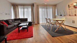 A modern living room with a sofa, coffee table, and dining area with chairs and a table. - Rue des Ixellois - 2 bedrooms (Liège)