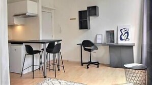 A compact living space with a kitchenette, two bar stools, a dining table, and a small side table with a framed picture.