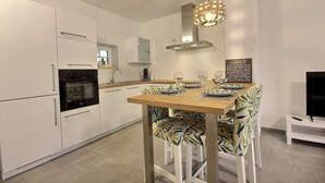 Een moderne keuken met witte kasten, een houten eettafel en gestreepte stoelen.