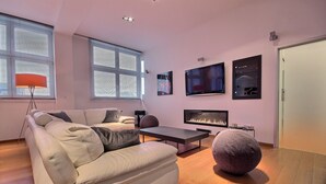 Una sala de estar moderna con un sofá color crema, un pouf redondo, una mesa de centro y una chimenea.