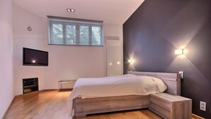 Un dormitorio moderno con una cama de madera, un televisor de pantalla plana, un calentador integrado y una ventana con persianas.
