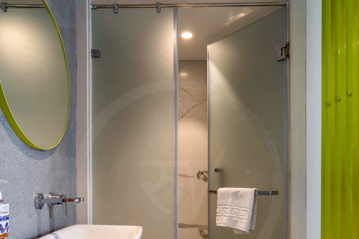 Un baño moderno con un lavamanos blanco, una cabina de ducha de vidrio y una pared de acento verde.