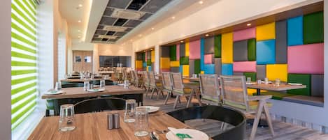 Un comedor moderno con varias mesas y sillas, un diseño de pared colorido y un techo con unidades de aire acondicionado.