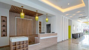 Una moderna zona de recepción con un mostrador de madera, un mostrador blanco y un área de descanso con sillas.