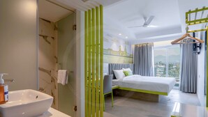 Habitación de hotel moderna con una cama grande, una mesita de noche, un baño con lavamanos y vistas a la ciudad.