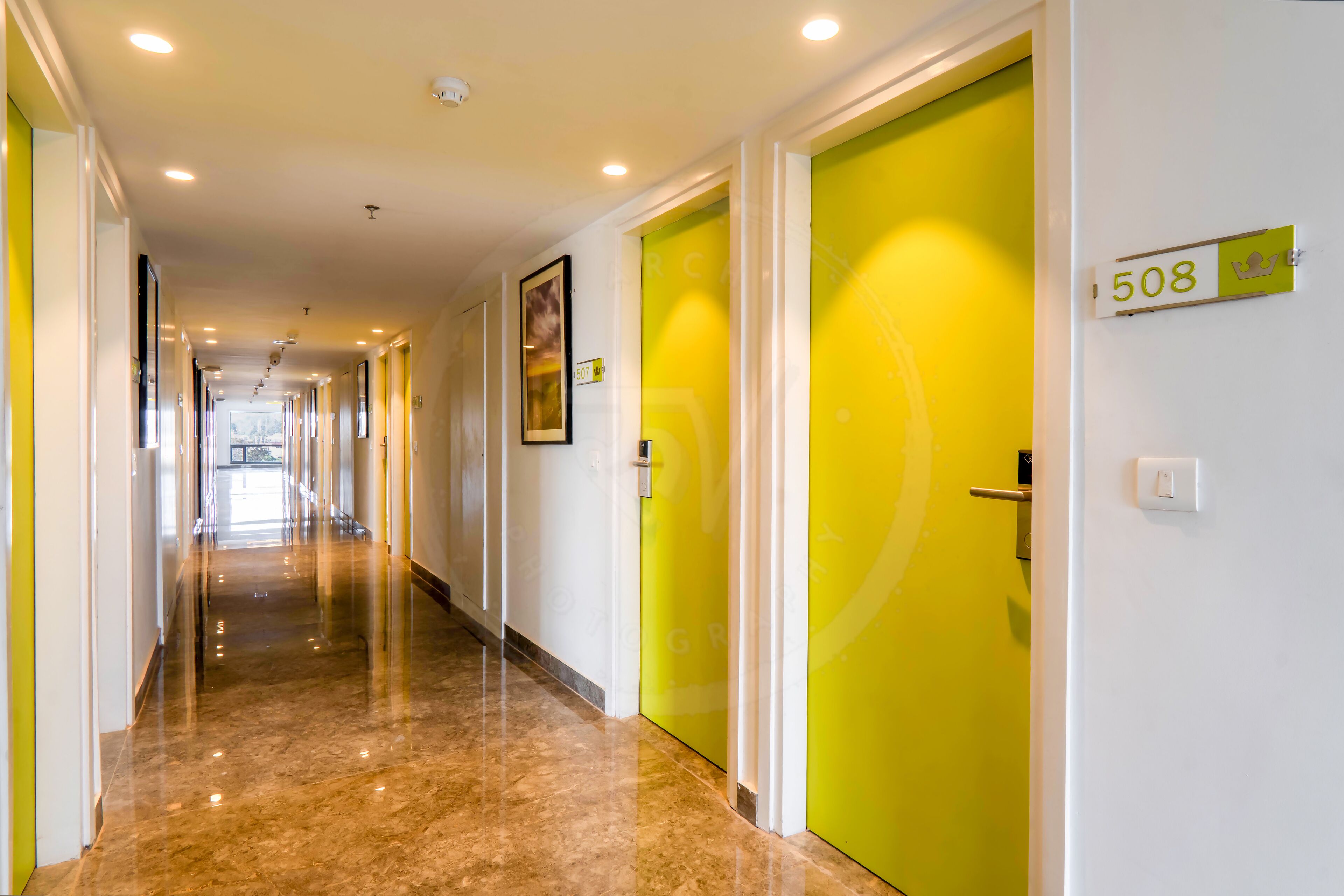 A hotel corridor with a bright yellow door marked 508, a polished marble floor, and recessed ceiling lights.