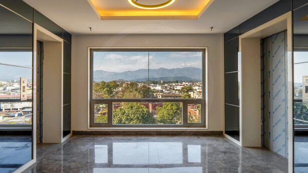 Amplia habitación con un ventanal que ofrece vistas panorámicas de la ciudad, suelo de mármol pulido e iluminación moderna de techo.