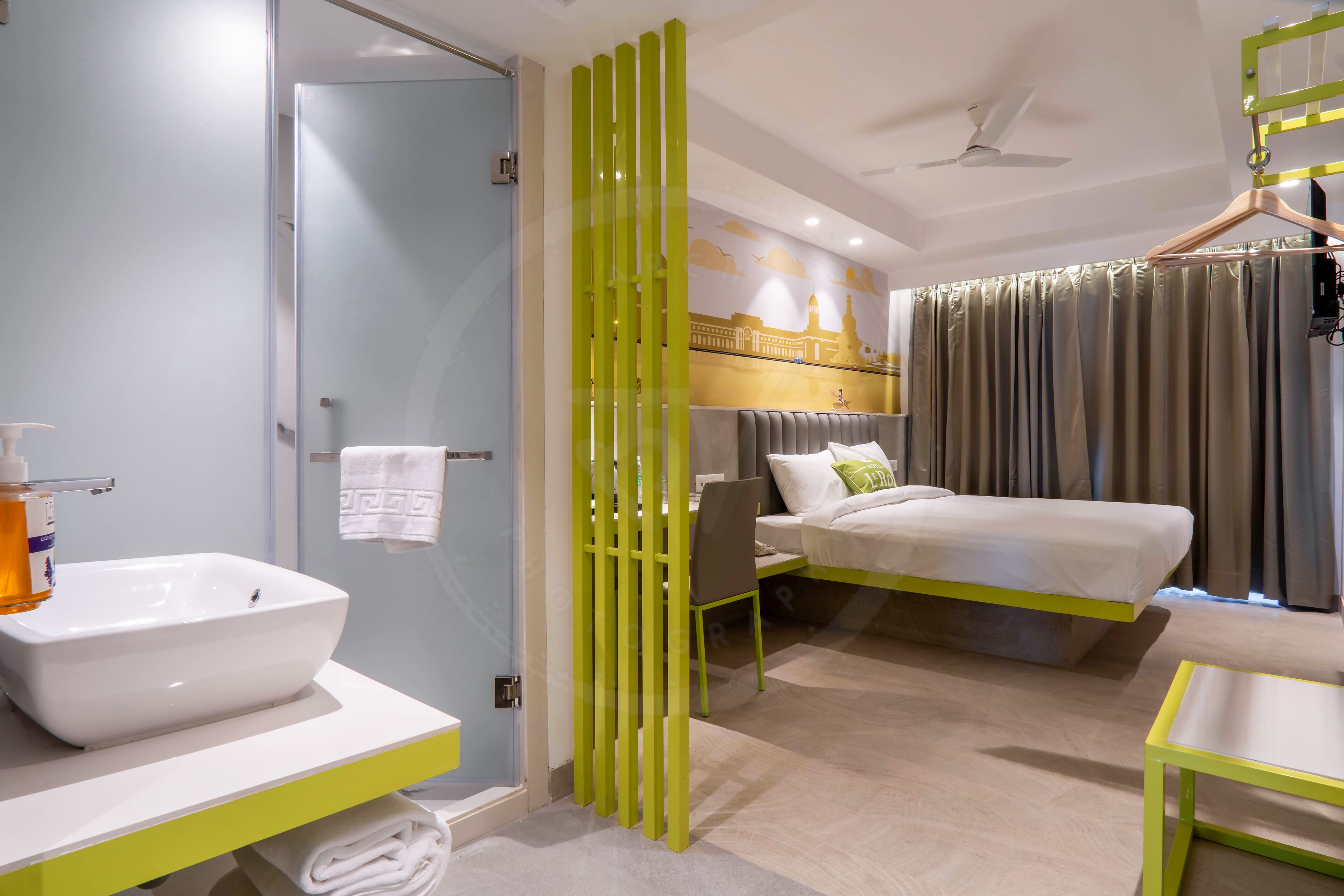 A modern hotel room with a large bed, a bedside table, a bathroom with a sink and mirror, and a shower area.