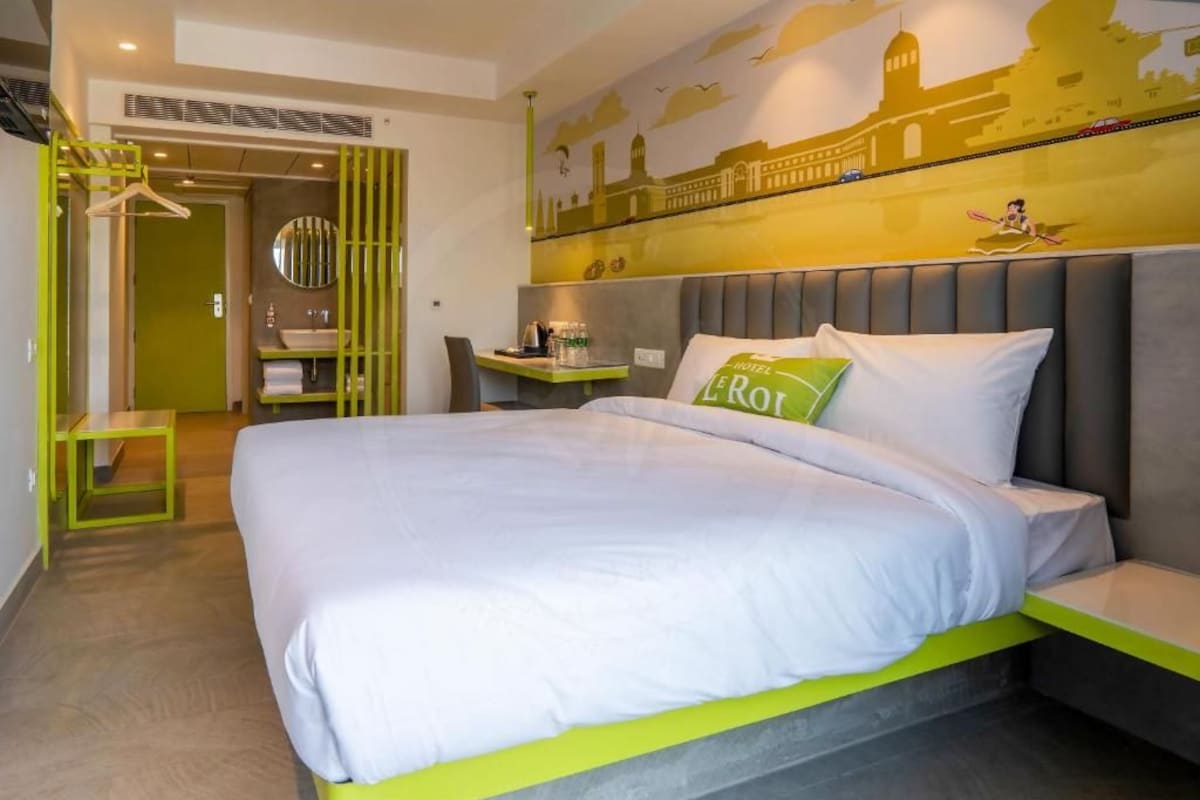 Een hotelkamer met een bed, nachtkastje, spiegel en een groene muur met een stadsgezichtsmural.