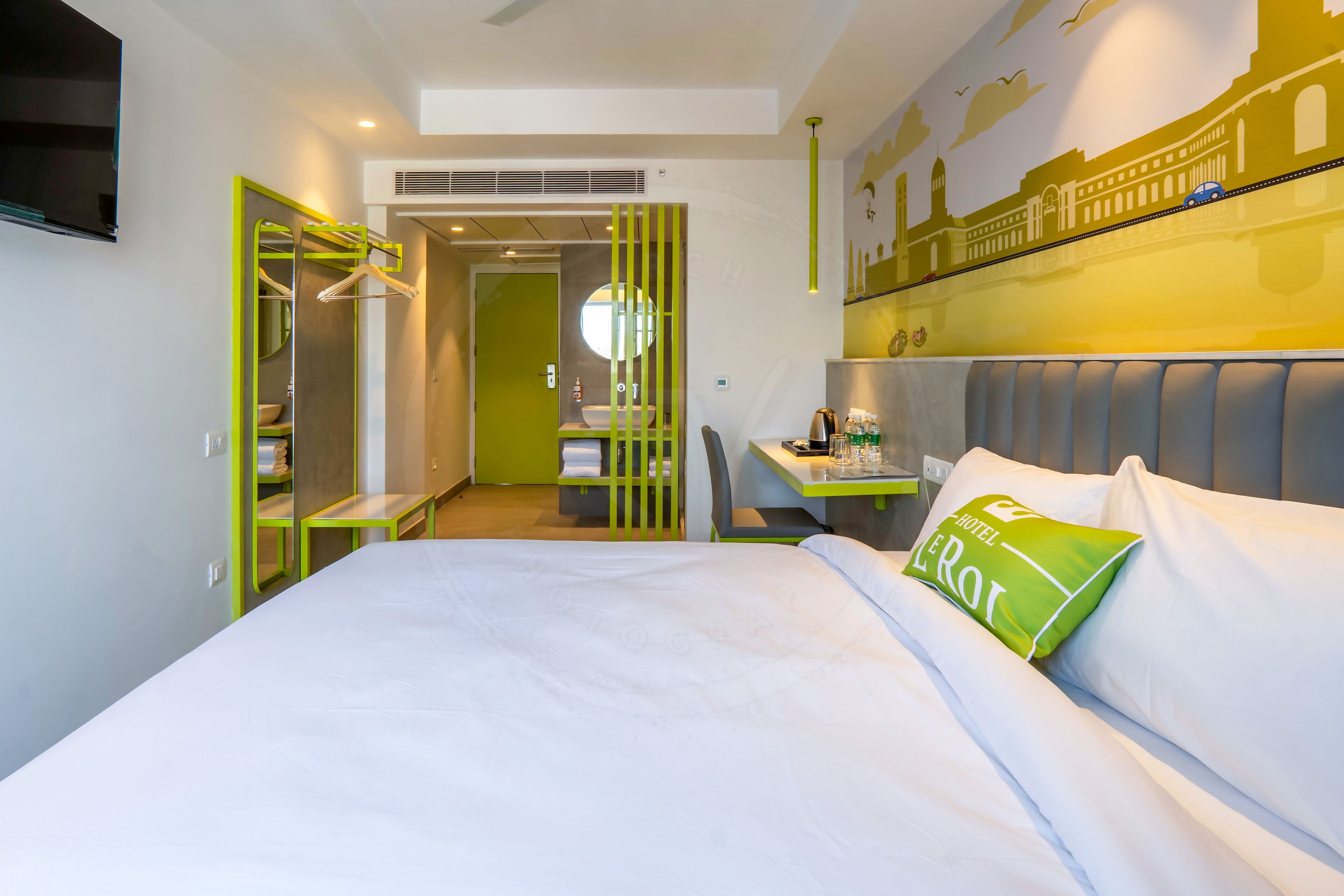 Habitación de hotel con cama, escritorio, silla, armario y baño visible a través de una puerta abierta.