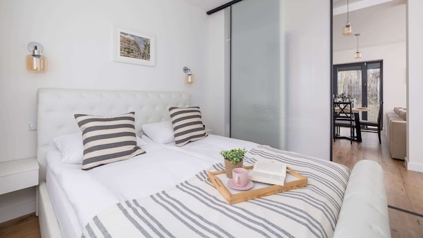 Un dormitorio moderno con una cama grande, ropa de cama a rayas, una mesita de noche, una lámpara de pared y una planta pequeña.