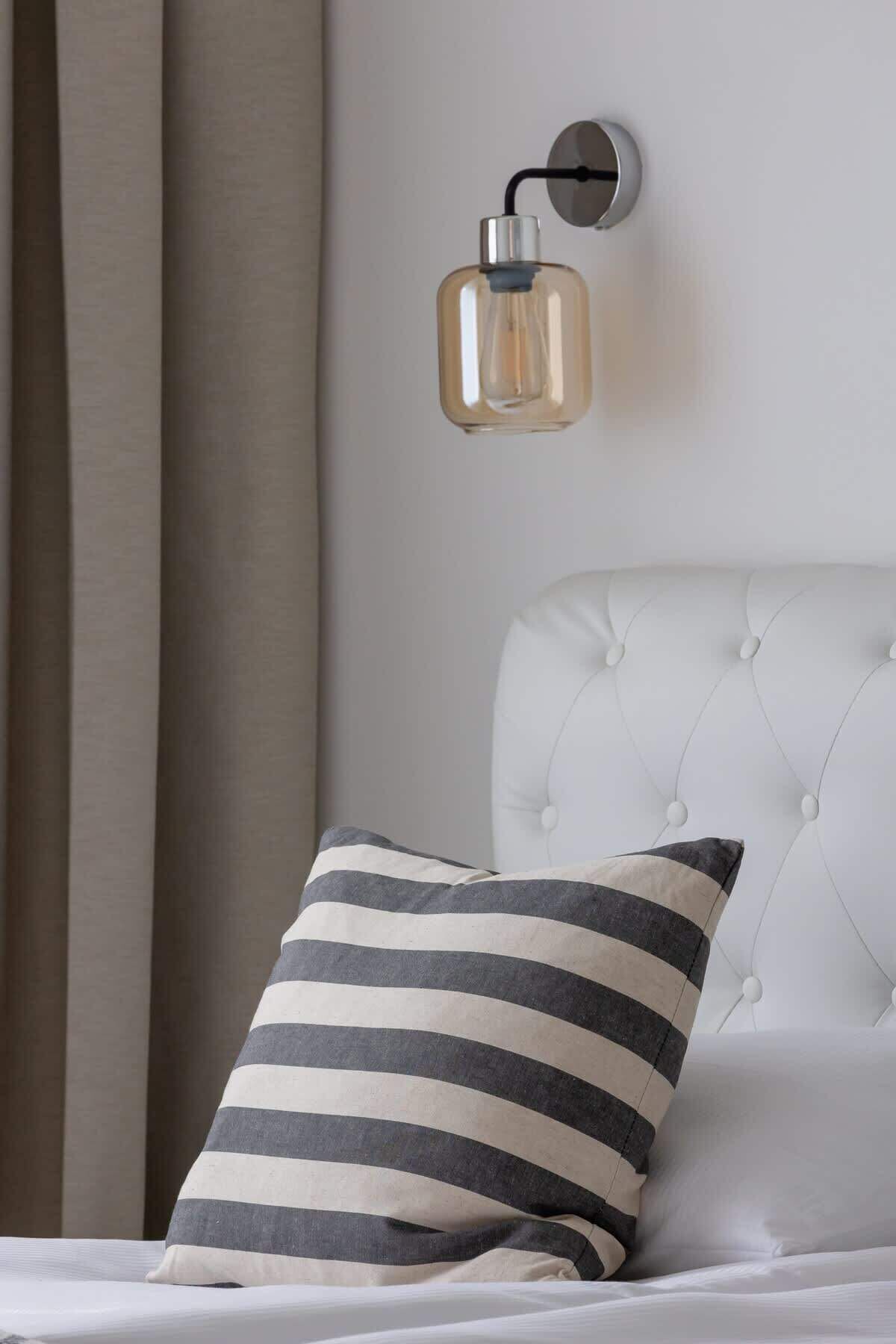 Quarto com cabeceira estofada, almofada listrada e luminária fixada na parede.