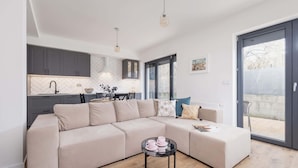 Una sala moderna con un sofá seccional color beige, una mesa de centro de vidrio y vistas a la cocina y al área exterior a través de una puerta corrediza de vidrio.