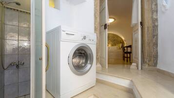 A laundry room with a front-loading washer and dryer, a shower, and a staircase leading to another room.