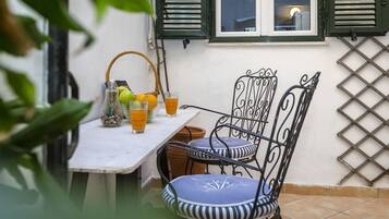 A patio with a table and two chairs, a basket with fruits, and a glass of orange juice.