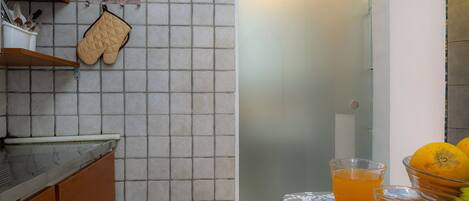 Una pequeña cocina con salpicadero de azulejos, armarios de madera y una mesa con mantel y bebidas.