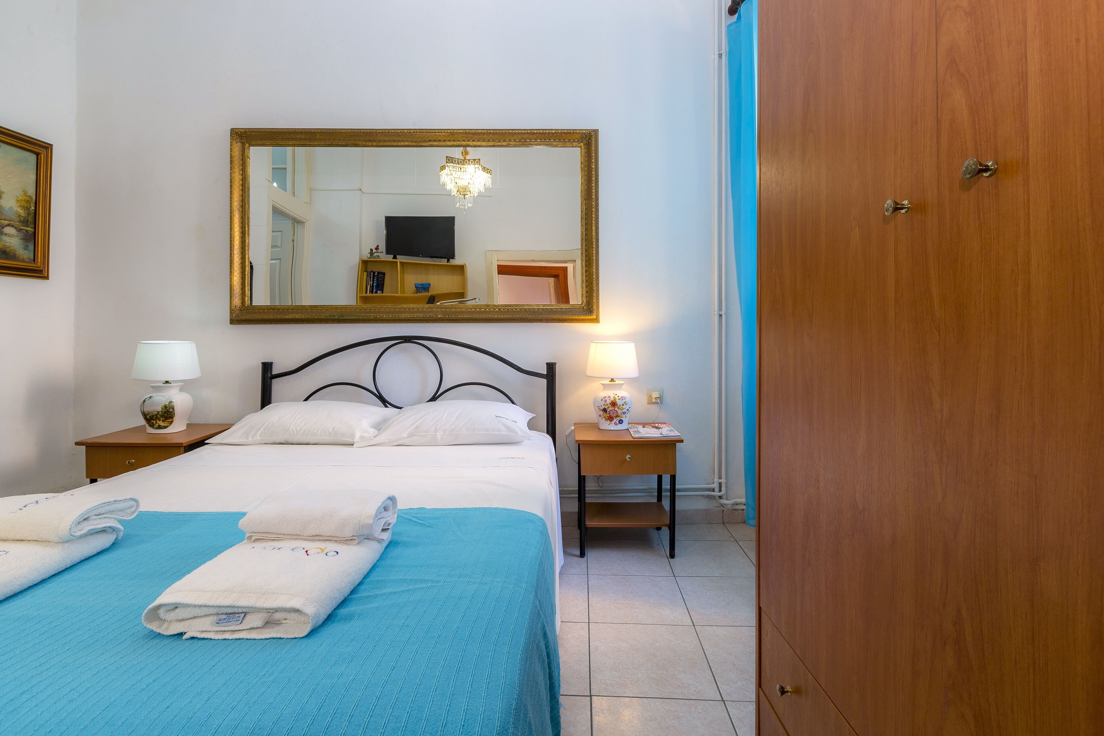 Una habitación de hotel con una cama, dos mesitas de noche, un tocador, un espejo y un armario.