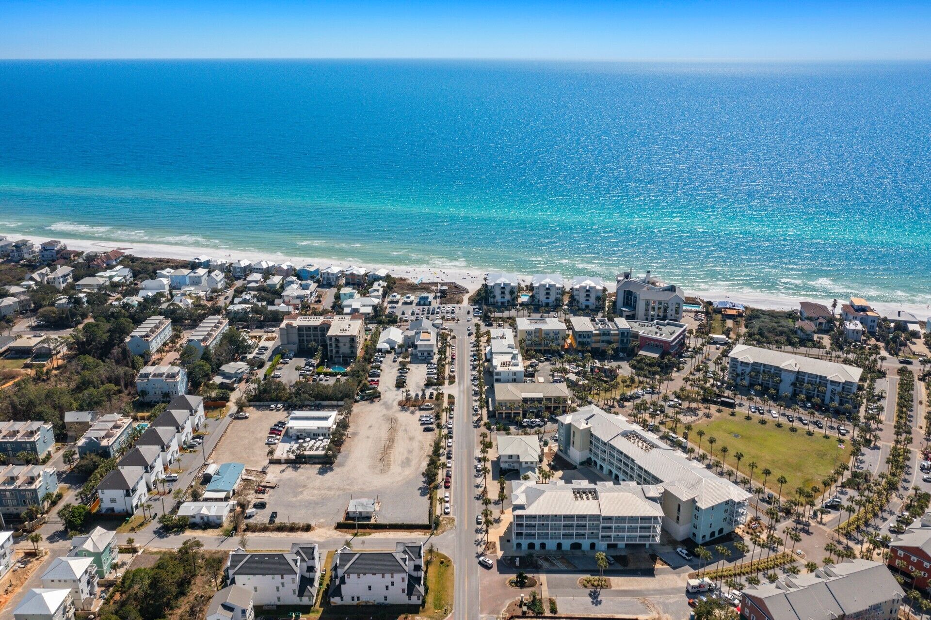 Vista aérea de una zona residencial costera con acceso a la playa, que muestra una combinación de casas unifamiliares y edificios de varios pisos, calles y zonas de estacionamiento.