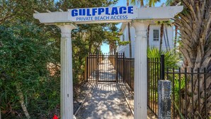 Een toegangshek naar Gulfplace Private Beach Access, met een duidelijk pad dat naar een wit gebouw leidt.