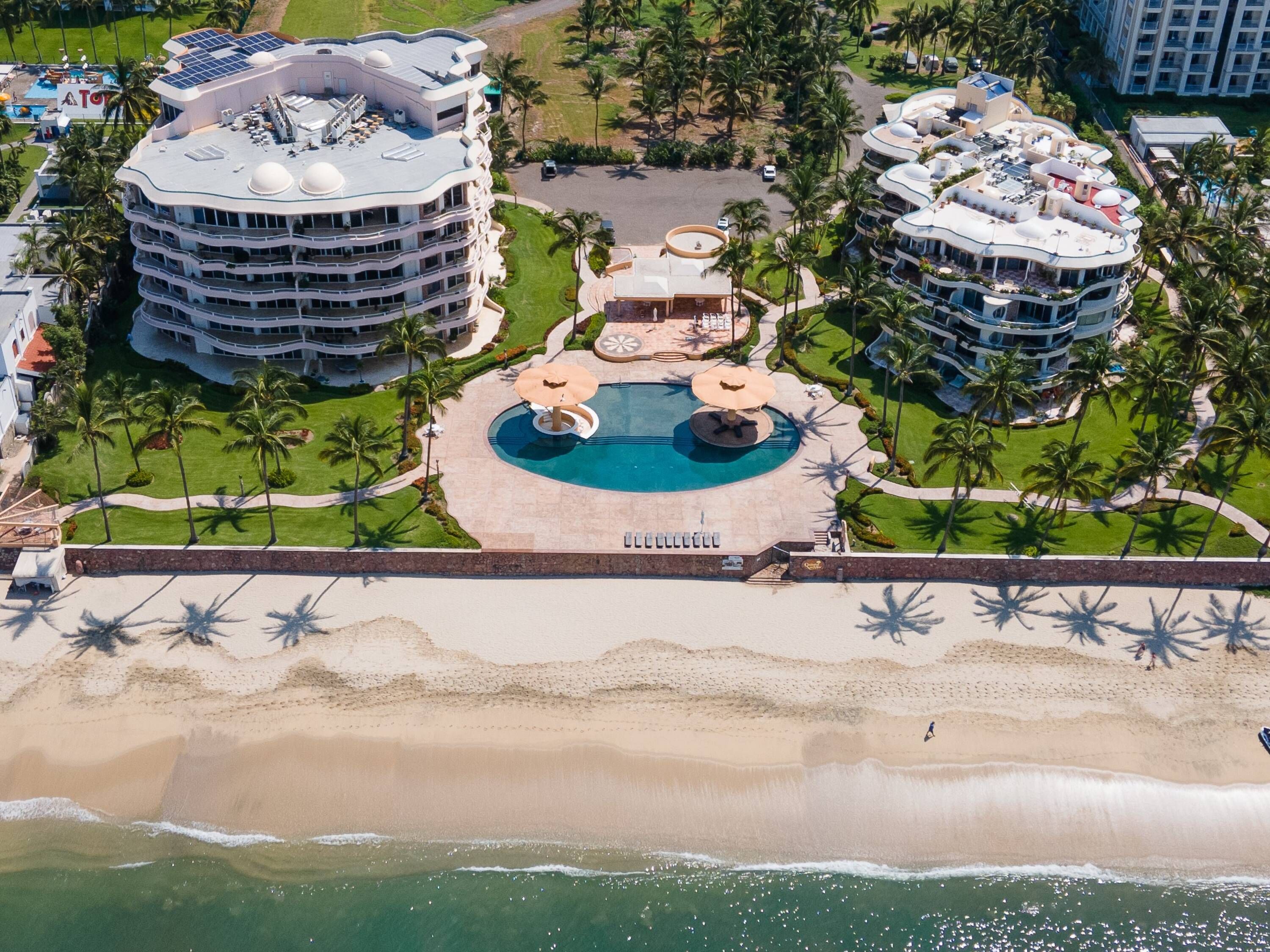 A resort with multiple buildings, a central pool area, and a beach.
