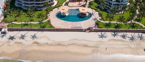 A resort with multiple buildings, a central pool area, and a beach.