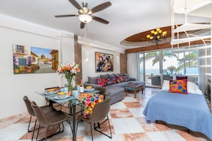 A well-lit living room with a dining area, a sofa set, and a bed with a view of the ocean.
