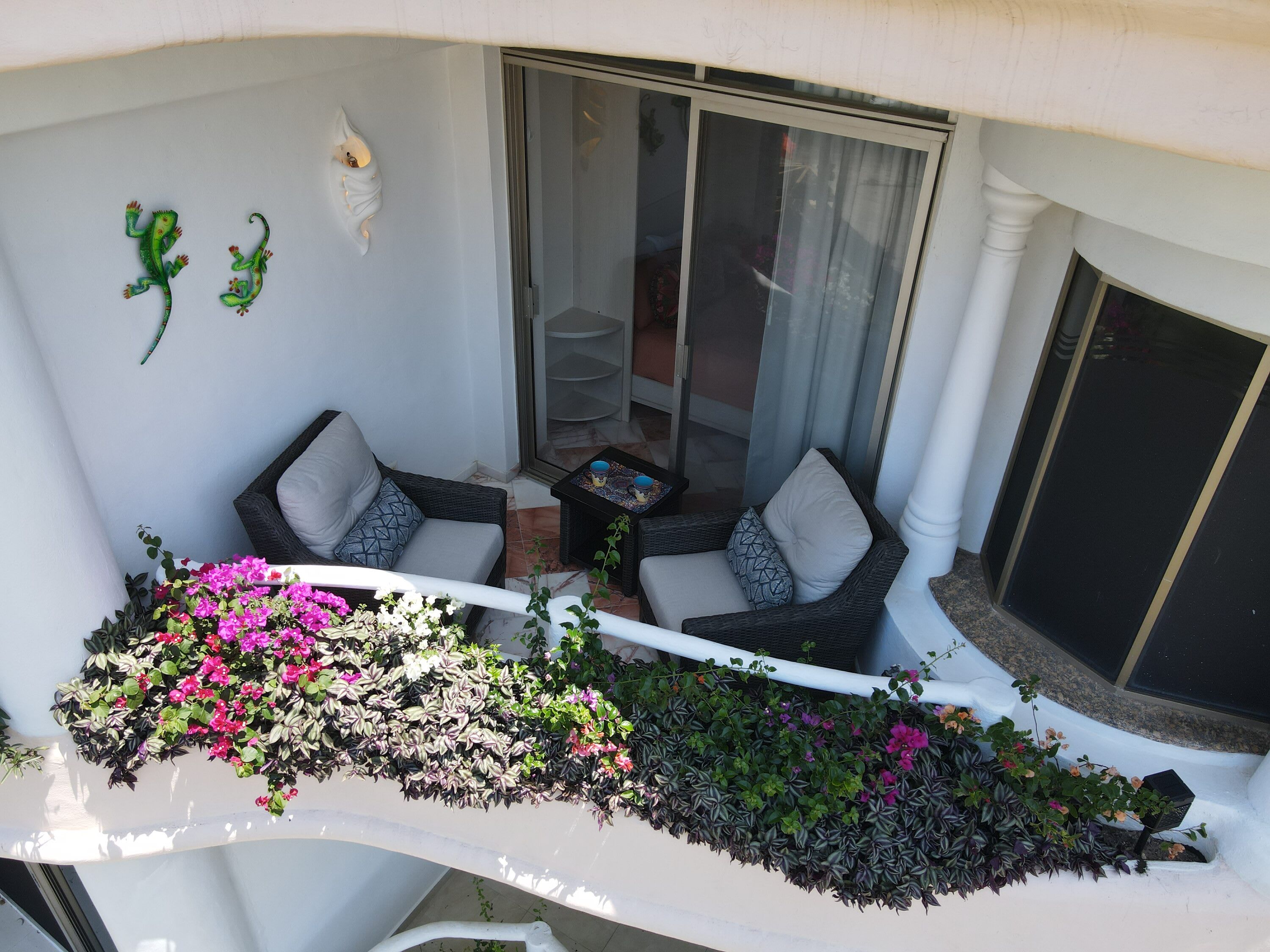 Un balcon agrémenté de deux canapés en osier, d’une petite table et de diverses plantes en pot.