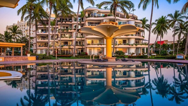 A hotel with a pool, palm trees, and a unique fountain structure.