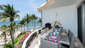 A balcony with a view of the beach and ocean, wicker furniture, and a table set for dining.