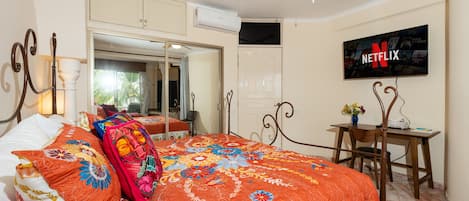 A bedroom with a bed, a desk, a television, and a ceiling fan.