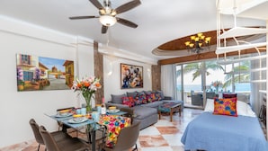 A spacious living area with a dining table, sofa, and bed, featuring a balcony with a view of the ocean.