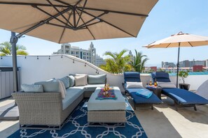 A rooftop lounge area with a sofa, lounge chairs, and umbrellas.